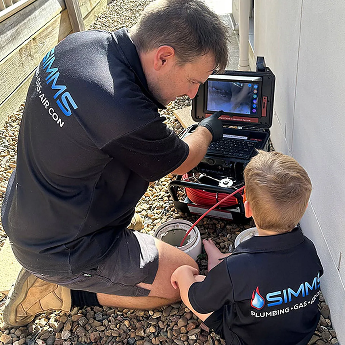 Daniel Simms and his son checking a drain camera screen together