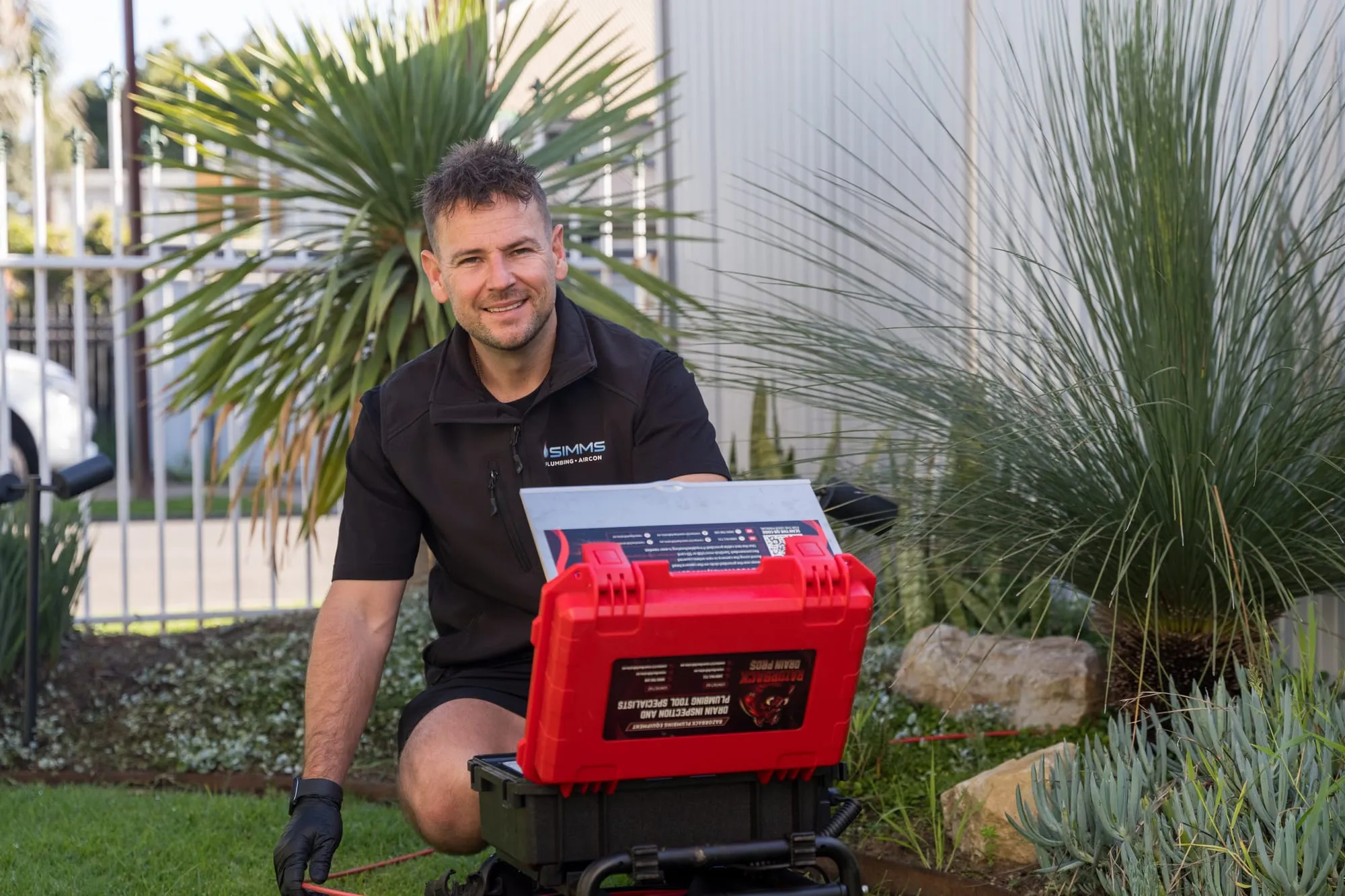Simms plumber kneeling beside a CCTV drain camera in a garden