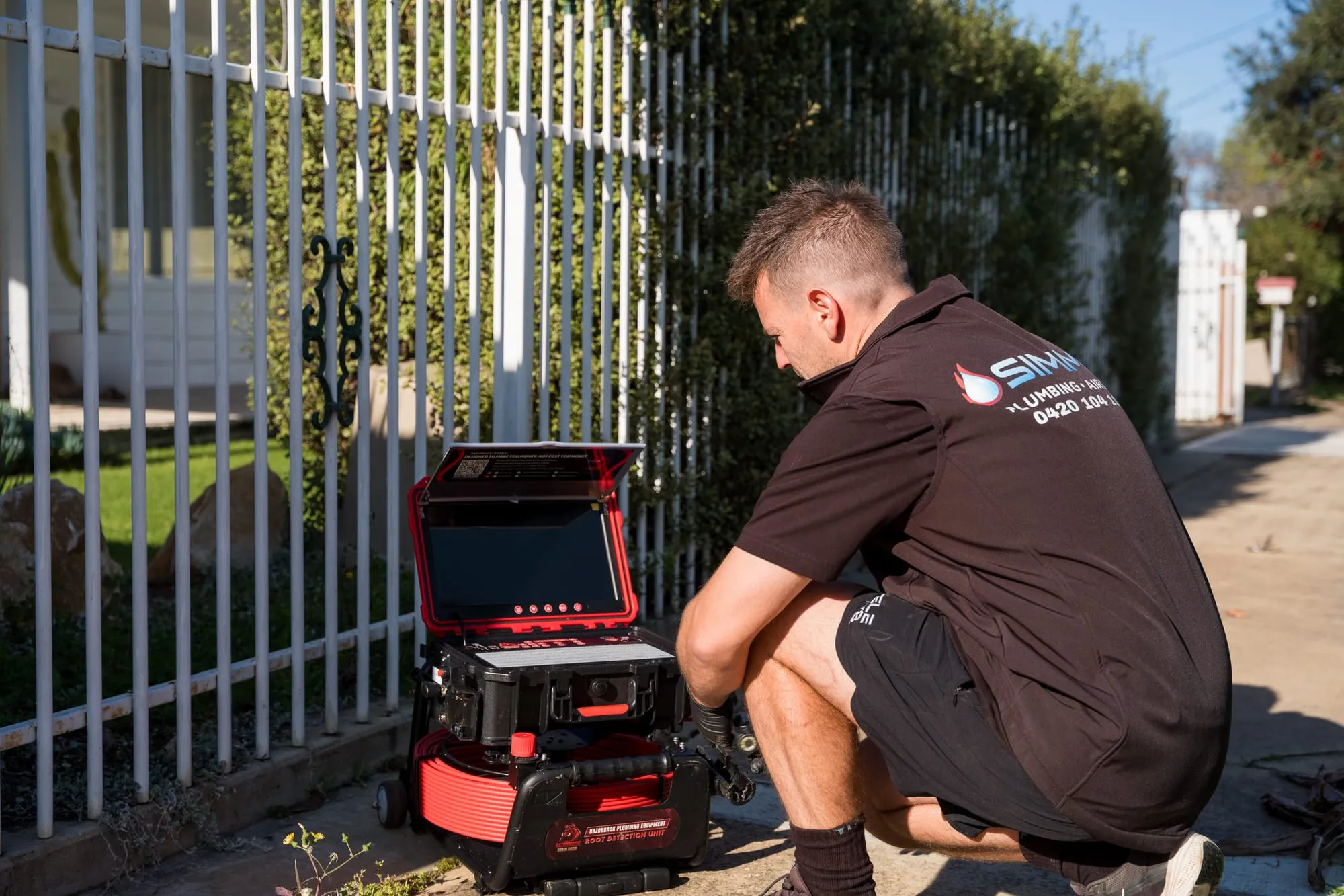Simms plumber inspecting a drain with a camera beside the footpath