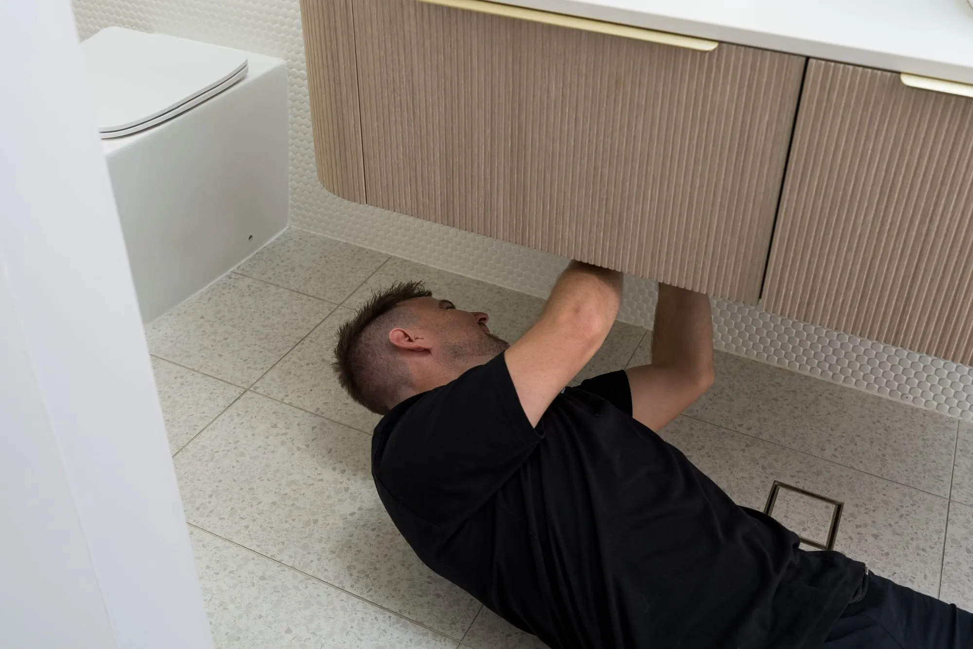 Simms plumber working on pipes under a bathroom vanity