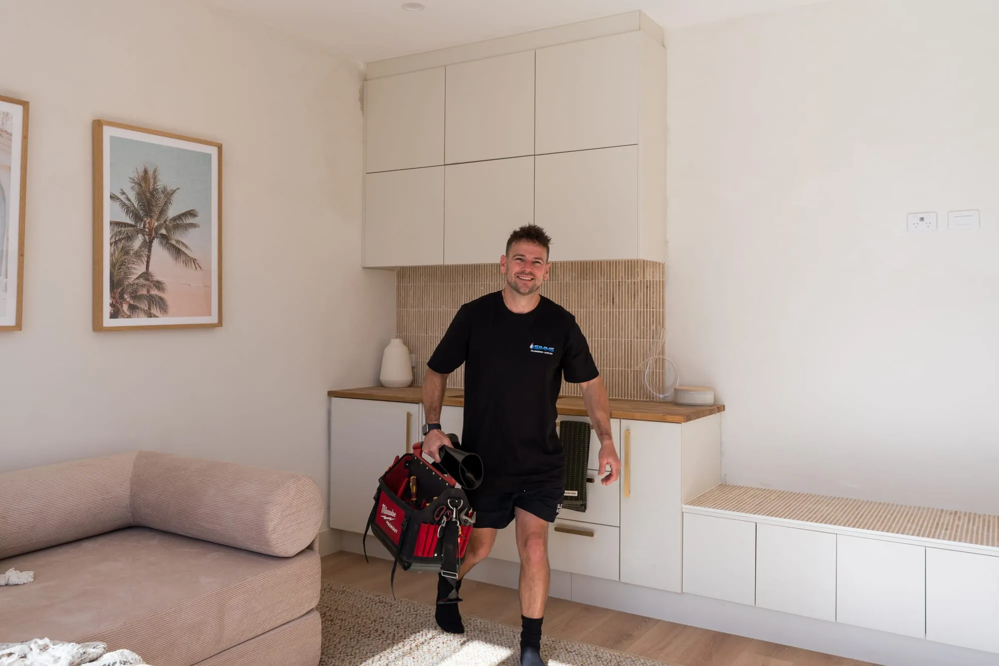 Simms plumber walking into a home carrying his toolbag